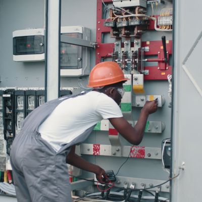 african-american-man-in-overalls-safety-helmet-and-glasses-working-on-switchgear-at-so-SBI-351269919